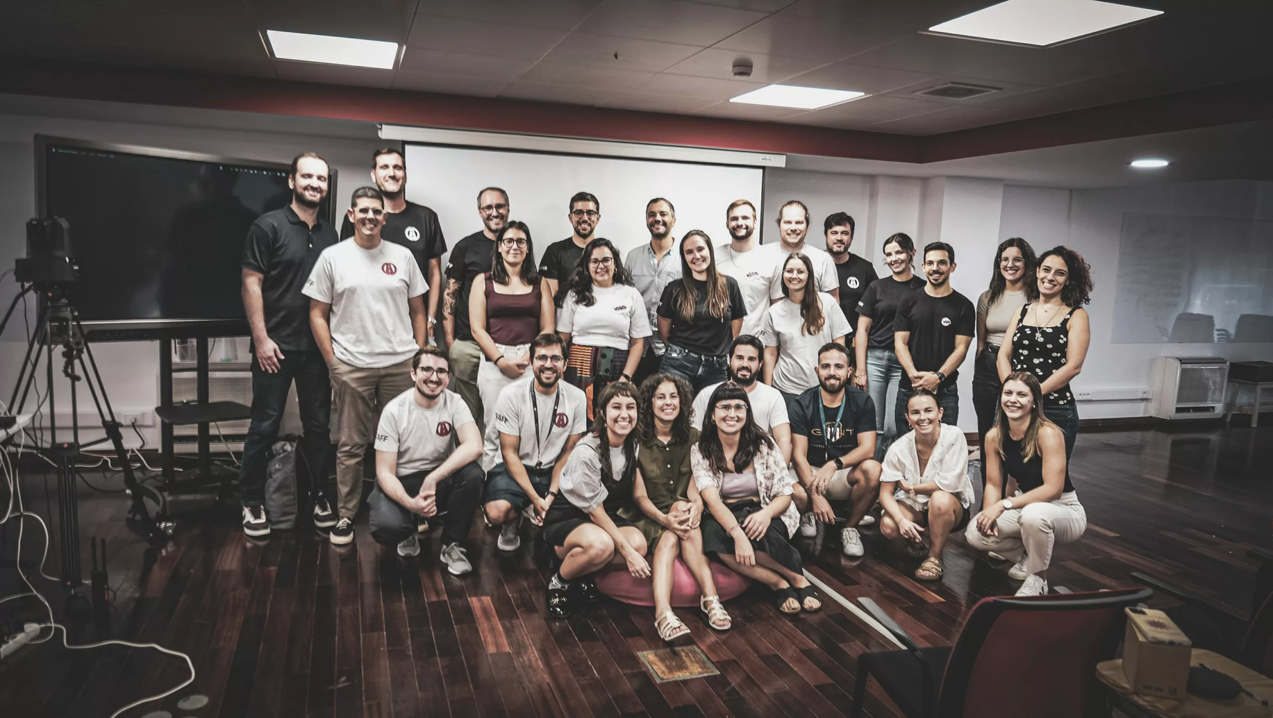 A group of people smiling and posing together in a room with a large screen.